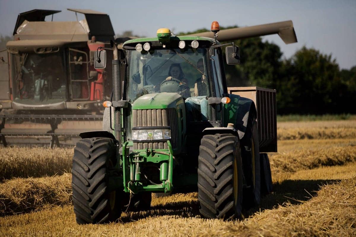A John Deere tractor and trailer running alongside a combine at harvest